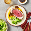 A gourmet meal of Beef Wellington is plated on a rustic dish with butternut squash puree and sautéed cabbage, viewed from above.