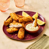 A maroon plate is filled with crispy, breaded chicken strips, served with a creamy dipping sauce and fresh lemon wedges.