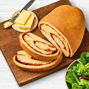 A loaf of savory swirl bread is sliced on a wooden cutting board, served with butter and a side salad.