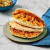 Two pita pockets filled with a carrot and raisin salad are stacked on a green plate, with a blue bowl in the background on a marble surface.