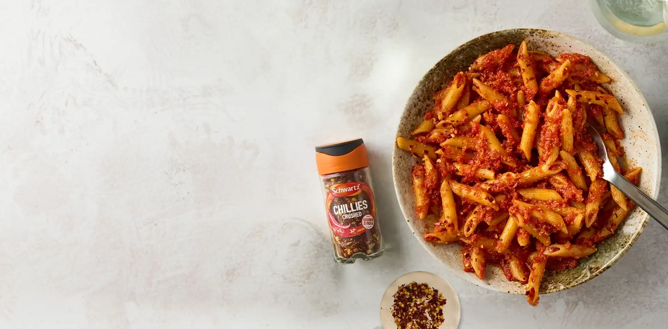 Pasta dish with a jar of chillies on a light gray background