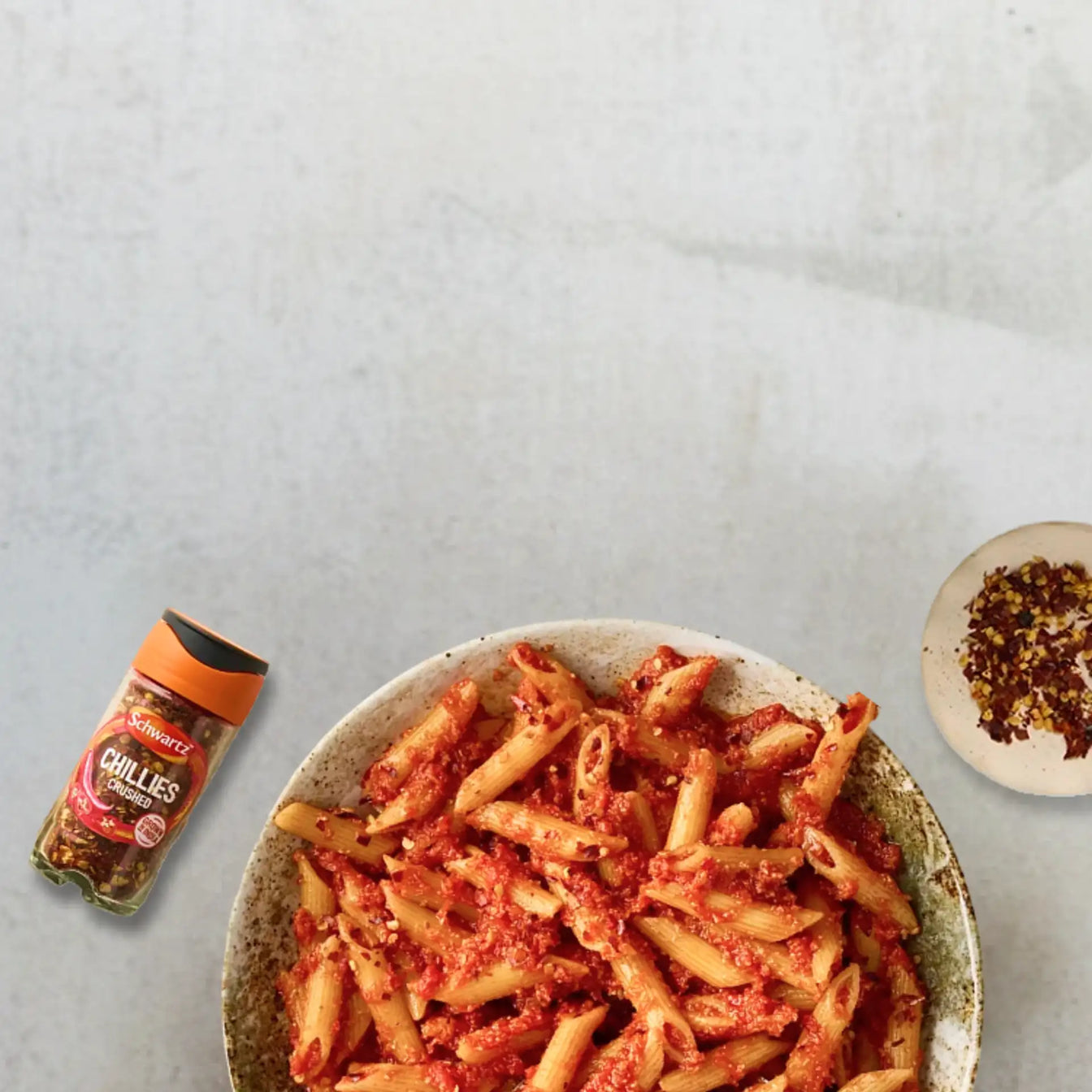 Pasta dish with a jar of chillies on a light gray background