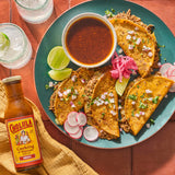 cholula birria cooking and simmer sauce next to a plate of birria tacos, juice, limes, pickled onions, and radishes