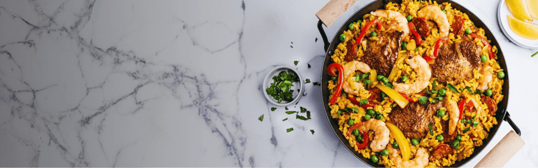 Paella dish with shrimp and vegetables in a skillet on a marble surface