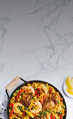 Paella with shrimp and vegetables in a pan on a marble surface