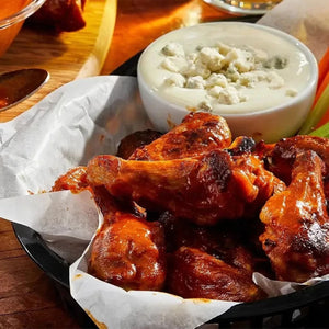 A basket of saucy chicken wings, made with a spicy sauce from the Barrel line, is served with a side of blue cheese dressing.