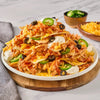 A large platter of chicken nachos is piled high with cheese, sour cream, olives, and jalapeños, with extra toppings served on the side in small wooden Barrel bowls.