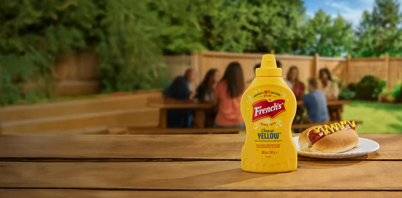 French's mustard bottle on a wooden table with a hot dog in the background