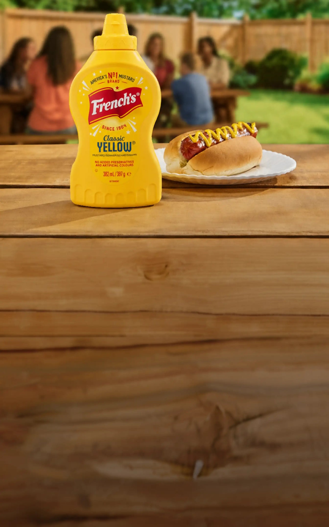 French's mustard bottle on a wooden table with a hot dog in the background