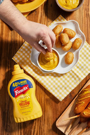 corn dog puffed dipped in classic yellow mustard on a picnic table