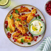 A plate of golden-brown fried halloumi sticks is garnished with pomegranate seeds, sliced red chili, and fresh cilantro, served with a creamy dipping sauce.