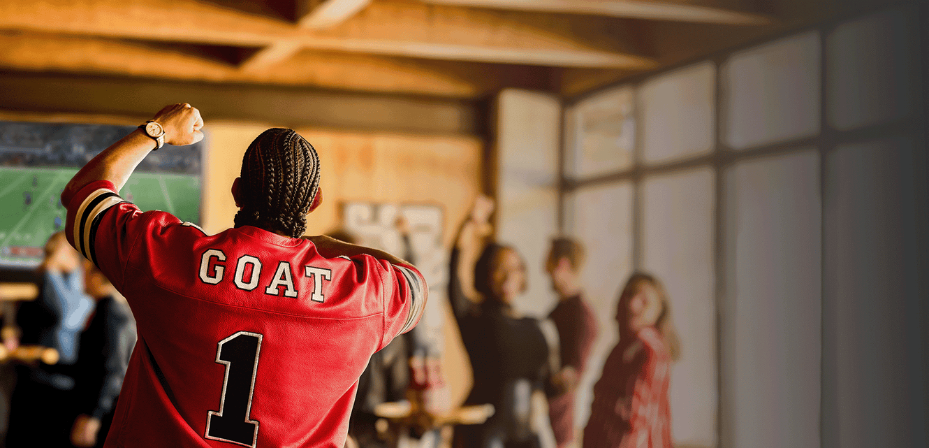 Person wearing a red jersey with 'GOAT' and number '1', standing in a room with people.