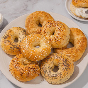 A variety of fresh bagels, including sesame, poppy seed, and everything, are piled on a plate, ready to be enjoyed as part of a delicious Barrel breakfast.