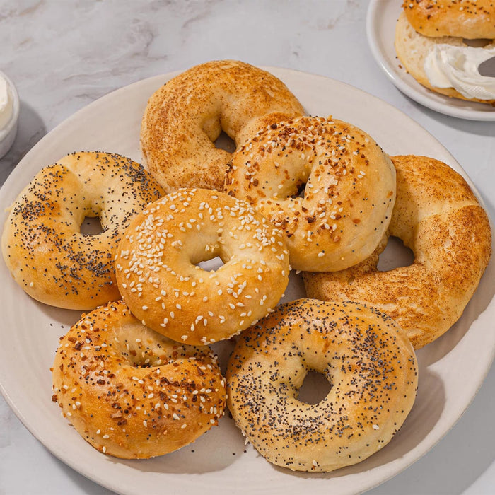 A variety of fresh bagels, including sesame, poppy seed, and everything, are piled on a plate, ready to be enjoyed as part of a delicious Barrel breakfast.