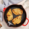 A top-down view shows three golden-brown, seasoned chicken cutlets cooking in a red and black cast iron Barrel skillet.