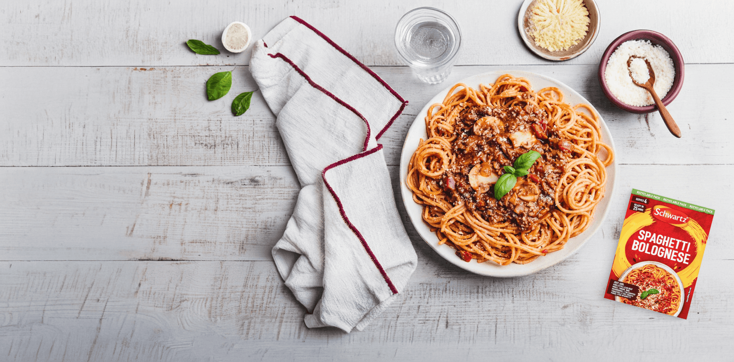 Spaghetti Bolognese with a package of Spaghetti Bolognese recipe mix on a wooden table.