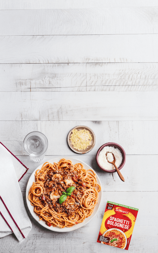 Spaghetti Bolognese with a package of Spaghetti Bolognese recipe mix on a wooden table.