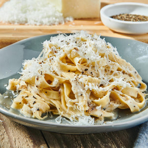 A plate of creamy fettuccine pasta is generously topped with freshly grated cheese and a sprinkle of Schwartz Medium Black Peppercorns 100G for a bold finish.