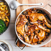 A delicious-looking meal of coq au vin is served in a large white pot, accompanied by a side of roasted potatoes and green beans.