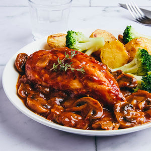 A plated meal of chicken breast smothered in a rich mushroom sauce and garnished with thyme, served with roasted potatoes and steamed broccoli.