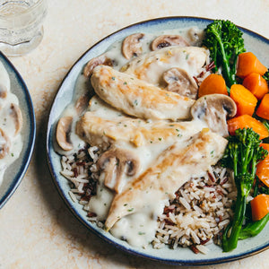 A delicious-looking meal of chicken tenders in a creamy mushroom sauce is served over wild rice with a side of broccolini and carrots.