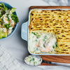 A delicious fish pie with a golden-brown mashed potato topping is served in a blue dish next to a fresh green salad.