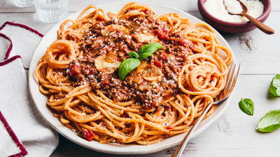 Platter of spaghetti with tomato sauce and basil on a wooden table.