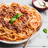 A heaping plate of spaghetti bolognese is garnished with fresh basil and grated cheese, with a fork resting on the side.