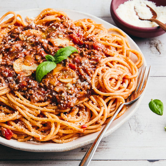 A heaping plate of spaghetti bolognese is garnished with fresh basil and grated cheese, with a fork resting on the side.