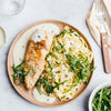 A beautifully plated dish of pan-seared chicken breast and tagliatelle pasta is served with a creamy white sauce and garnished with fresh arugula and black pepper.