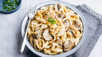 Pasta dish with mushrooms in a creamy sauce on a white plate, garnished with parsley.