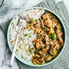 A delicious-looking bowl of creamy mushroom stew is served alongside wild rice and garnished with fresh parsley and black pepper.