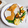 A plated roast pork dinner with gravy, green beans, roasted potatoes, and applesauce is shown from above on a wooden table.