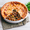 A golden-brown, flaky meat pie sits in a white dish, with a portion of the crust broken open to reveal a savory filling of minced meat, carrots, and celery.
