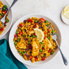 Two white bowls are filled with a savory chicken and rice dish, mixed with peas and red peppers, and garnished with a lemon wedge.