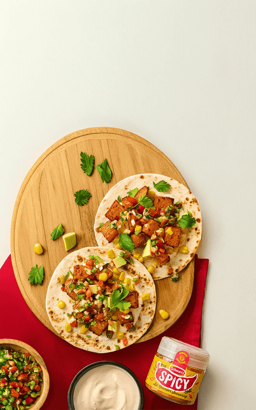 Tortillas with toppings on a wooden board, accompanied by a bowl of salad, sour cream, and a jar of spicy all rounder seasoning. 