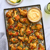 A baking sheet is filled with golden-brown chicken wings, garnished with peanuts, red chili, and cilantro, and served with a creamy dipping sauce.