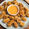 A plate of golden-brown Barrel chicken nuggets are arranged around a central bowl of creamy orange dipping sauce.