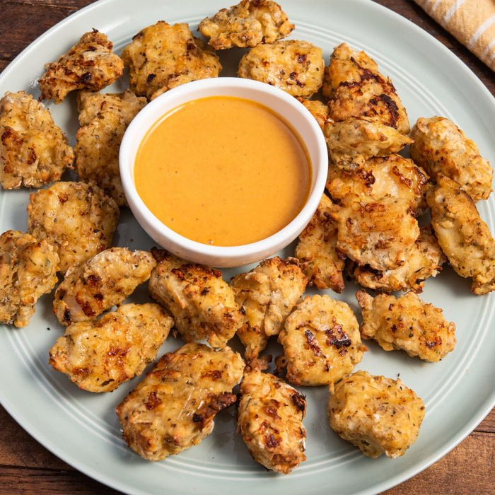 A plate of golden-brown Barrel chicken nuggets are arranged around a central bowl of creamy orange dipping sauce.