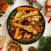 A festive green bowl of roasted root vegetables, seasoned with a flavorful Barrel blend and topped with hazelnuts, is surrounded by holiday decorations.