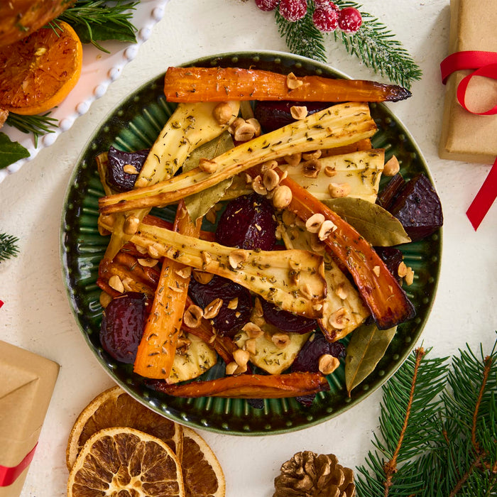 A festive green bowl of roasted root vegetables, seasoned with a flavorful Barrel blend and topped with hazelnuts, is surrounded by holiday decorations.