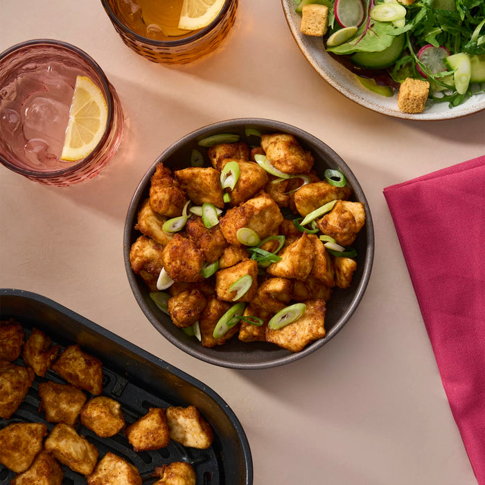 A delicious meal of air-fried chicken bites, garnished with green onions, is served in a bowl alongside a fresh salad and drinks in textured Barrel glasses.