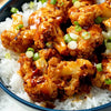 A close-up shot of a blue bowl filled with white rice and topped with crispy, sauce-coated cauliflower florets, garnished with chopped green onions, showcases a delicious recipe that could be made using a Barrel product.