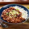 A delicious bowl of Barrel chili con carne is served with white rice and topped with cheese and green onions.