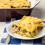 Cheesy casserole with chicken and broccoli on a white plate with a fork, on a blue and white checkered tablecloth.