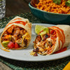 Two delicious Barrel chicken burritos are cut in half on a plate, showing a filling of grilled chicken, avocado, cheese, and black beans, with a side of Spanish rice in the background.