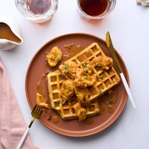 An overhead shot shows a delicious plate of chicken and waffles with gravy, served alongside drinks in a stylish Barrel glass.