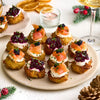 A festive platter of potato latke appetizers, some topped with smoked salmon and caviar and others with beetroot relish, is served alongside a glass of wine that could be from a Barrel.