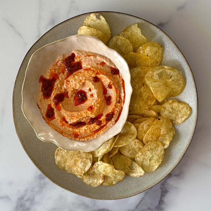 A top-down view of a bowl of creamy Barrel dip topped with chili sauce, served on a rustic plate with potato chips.