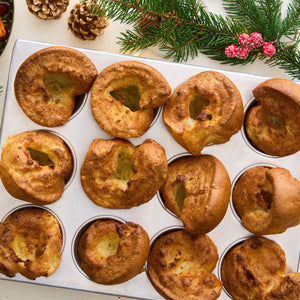 A top-down view shows freshly baked Yorkshire puddings, with their golden-brown puffed Barrel shape, resting in a muffin tin amidst festive holiday decorations.